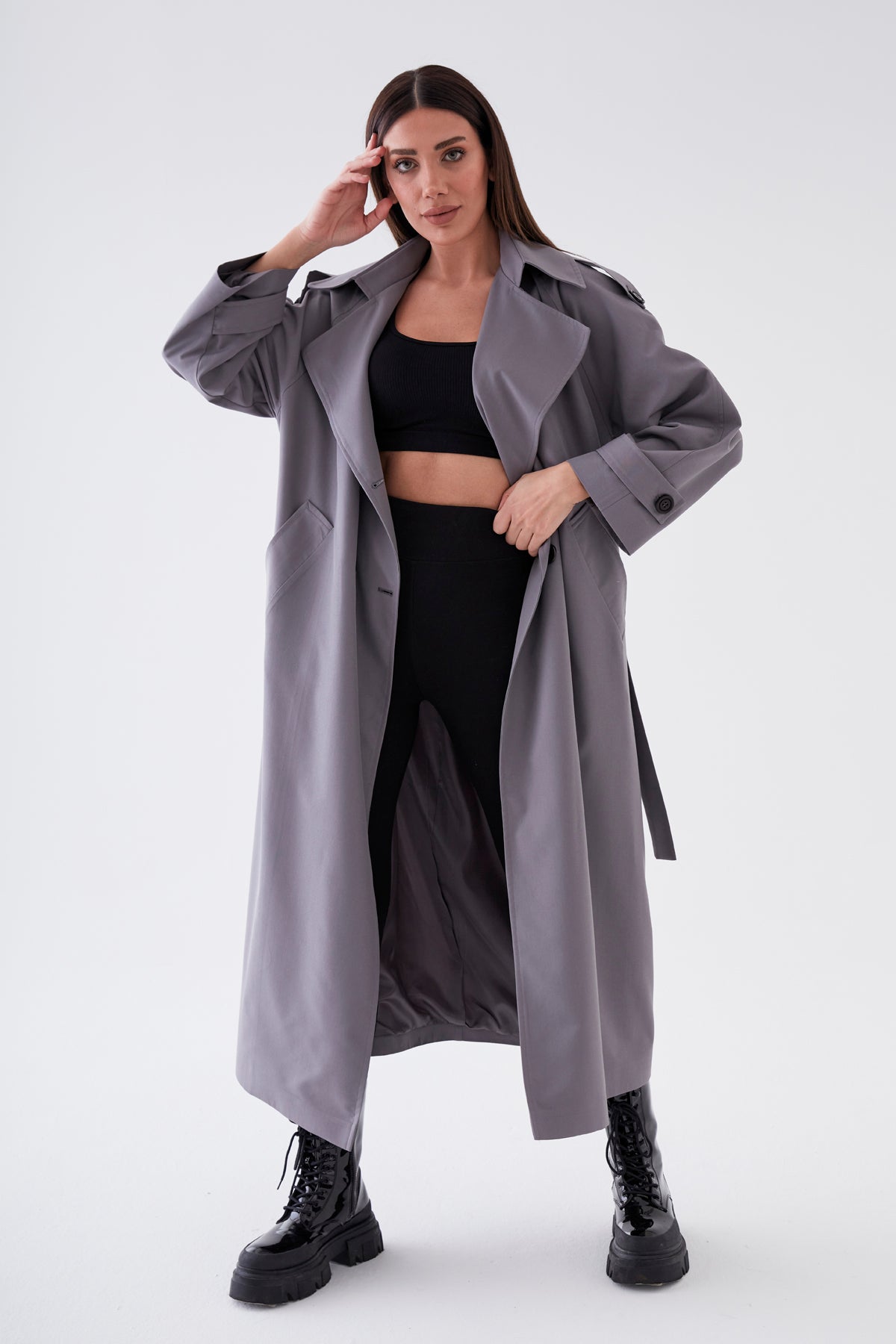 Woman wearing a long gray coat over black athletic wear on a white background