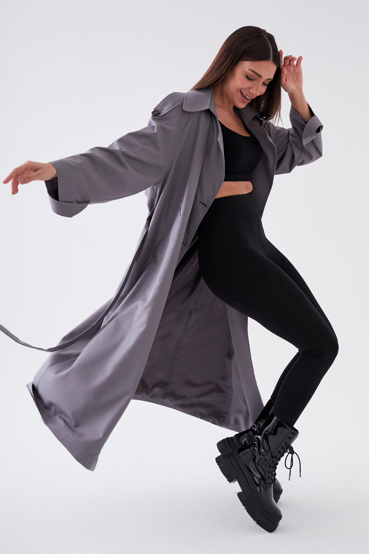 Woman in a gray coat and black outfit posing on a white background