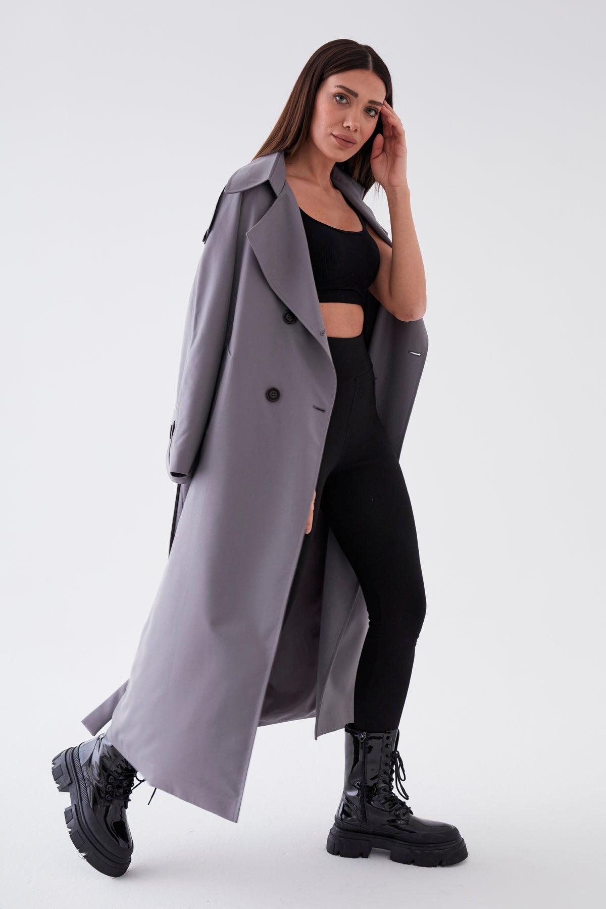 Woman wearing a long gray coat over a black outfit on a white background