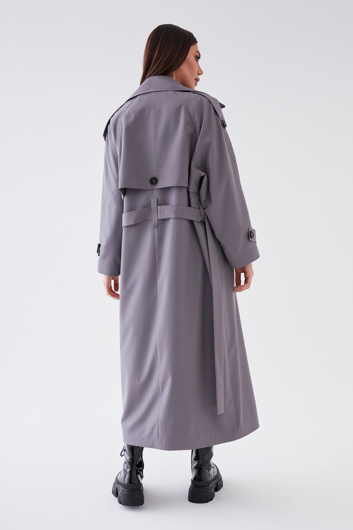 Woman wearing a long gray trench coat on a white background