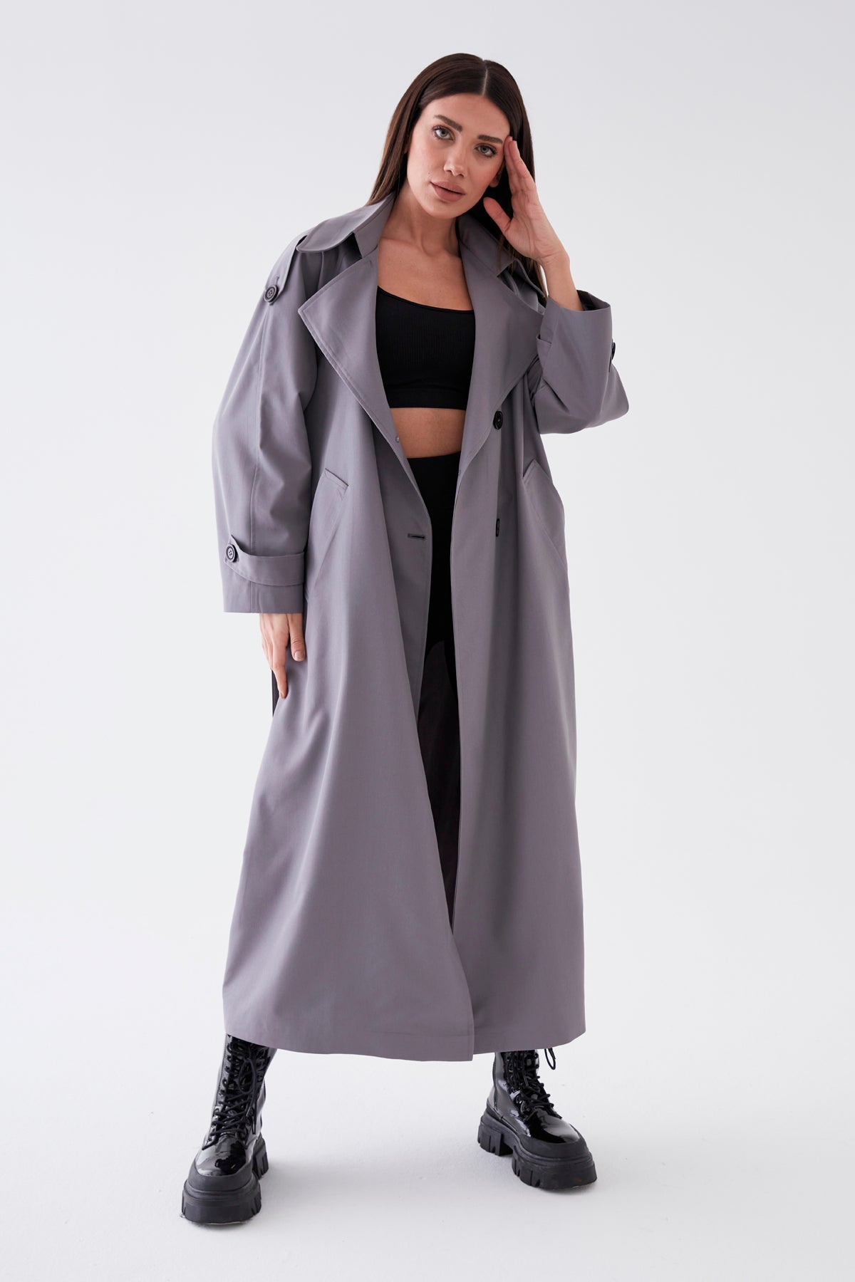 Woman wearing a long gray coat over a black outfit on a white background