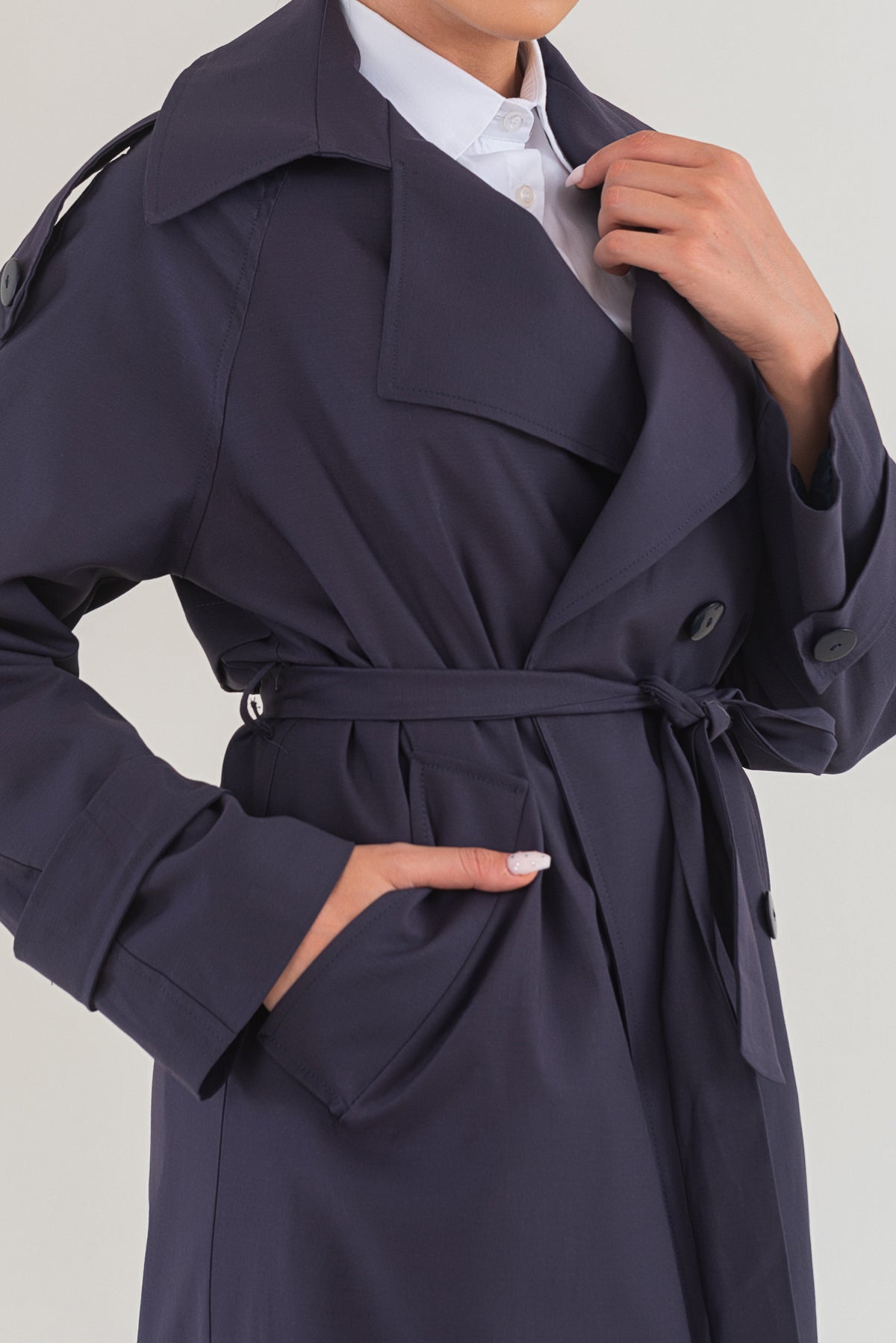 Navy trench coat worn by a person on a light gray background