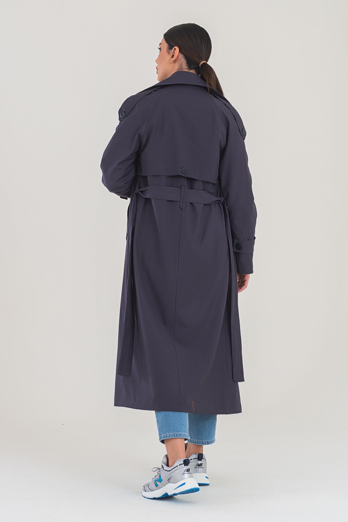Person wearing a long dark coat on a plain background