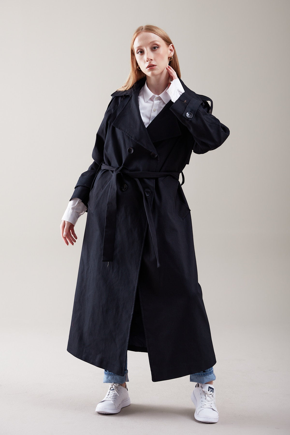 Woman wearing a black trench coat on a plain background