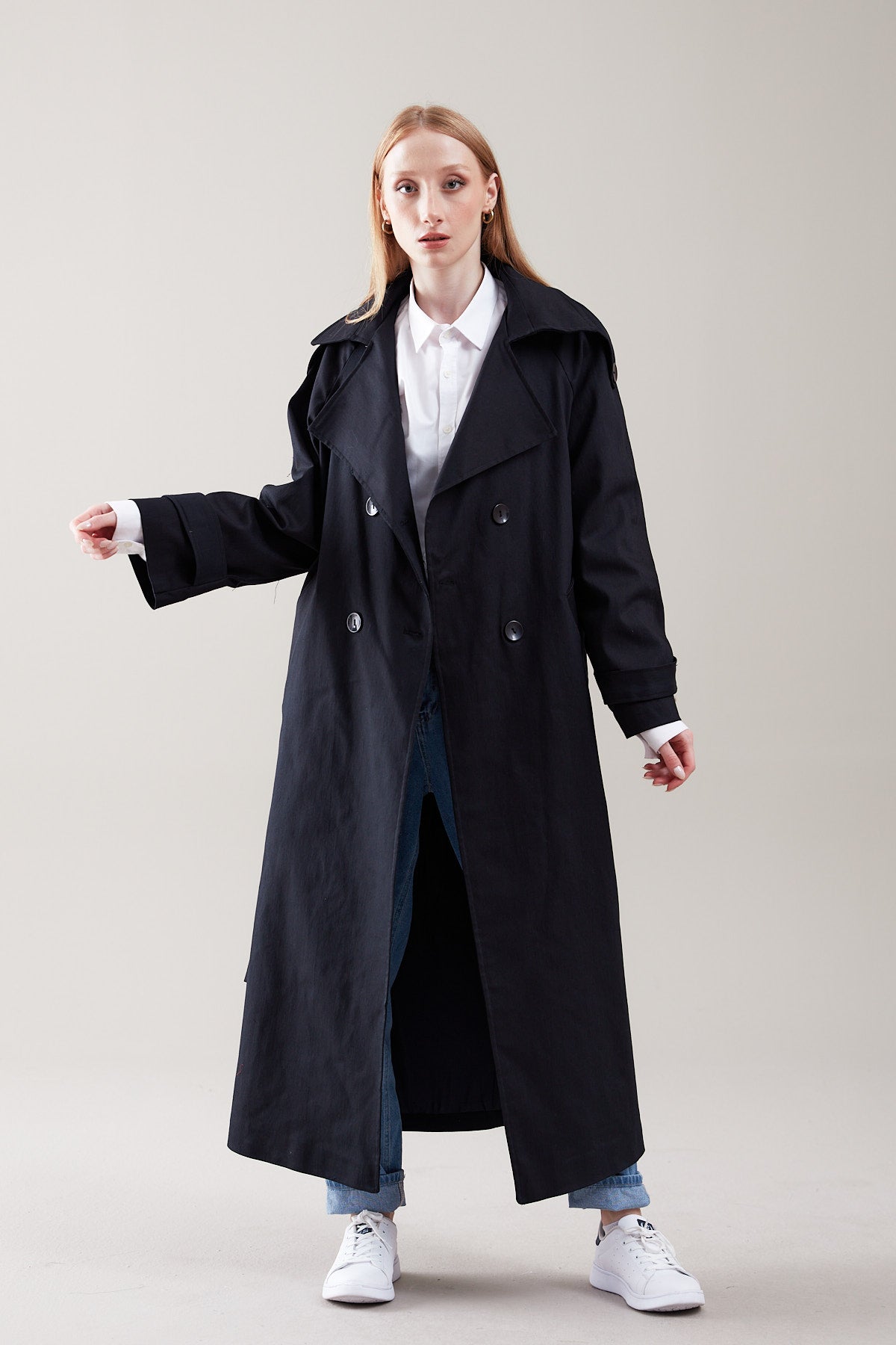 Woman wearing a long black coat over a white shirt on a plain background