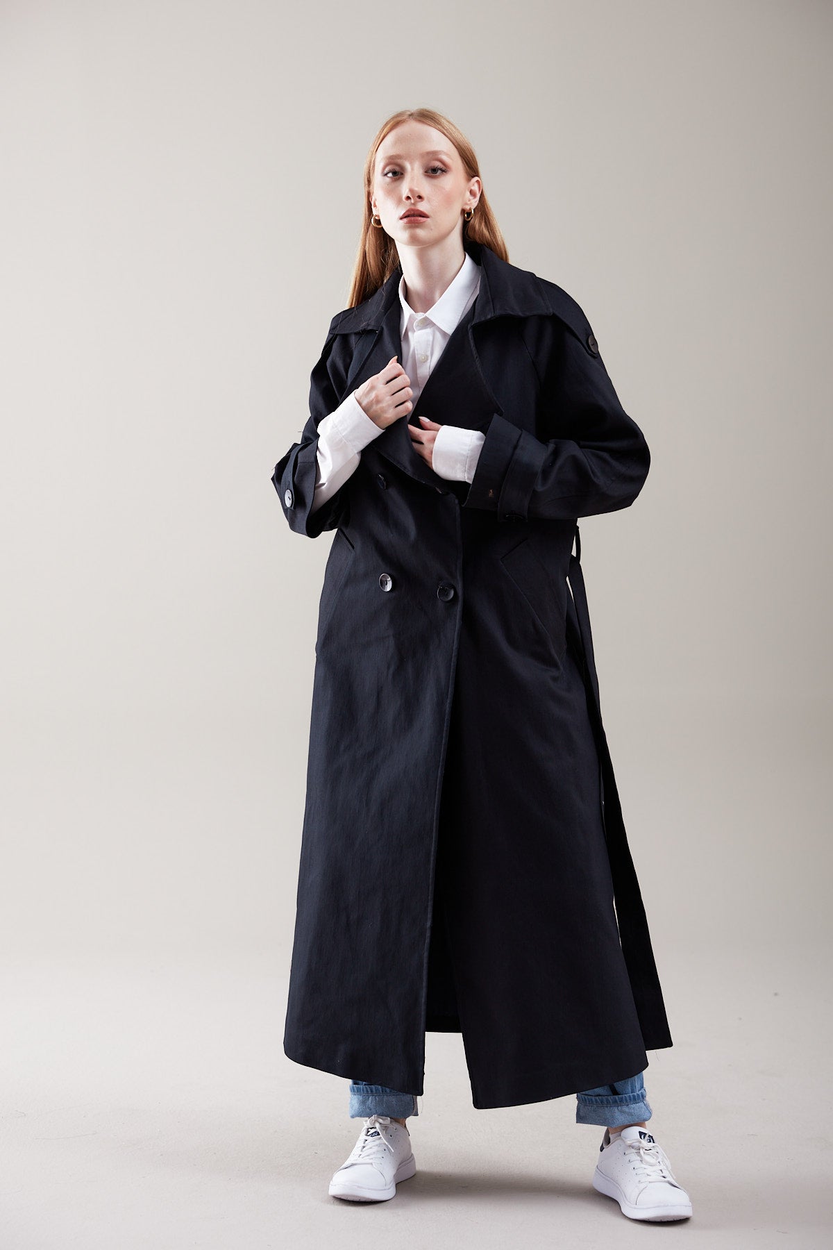 Person wearing a long black coat on a plain background