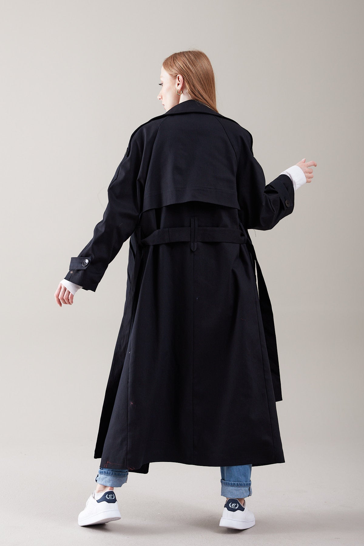 Person wearing a long black coat on a plain background